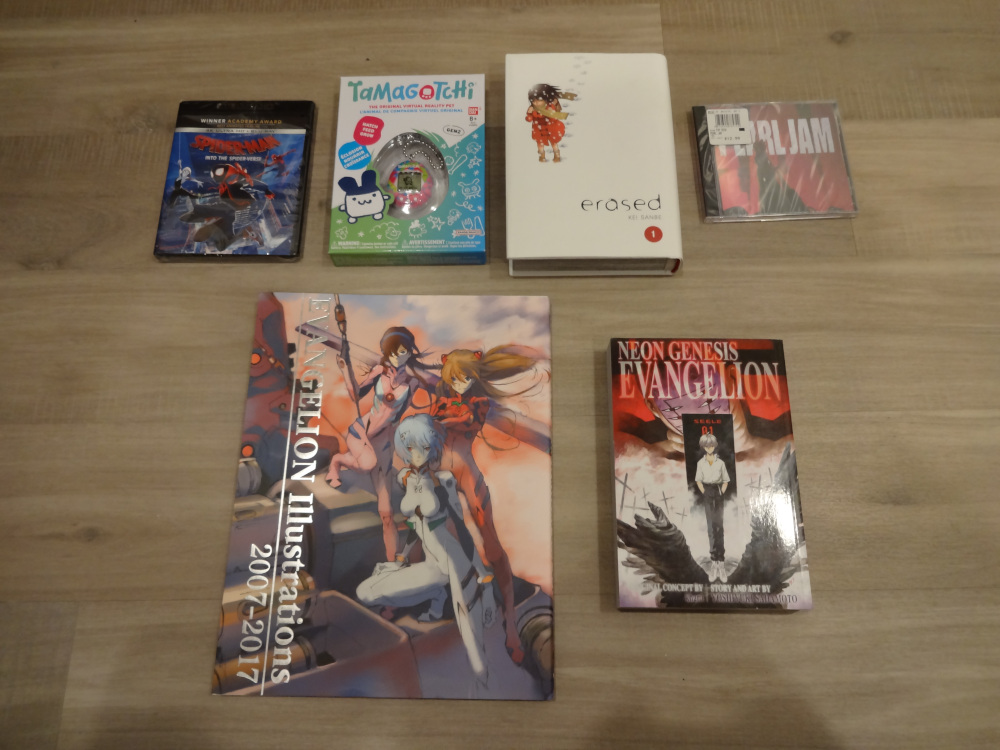 Spiderman: Into the Spider-Verse on 4K Blu-Ray, a Gen 2 Tamagotchi, erased Vol 1 Hardcover, a CD of Ten by Pearl Jam, an Evangelion art book, and another Evangelion omnibus
